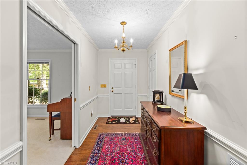 Furnished hallway with a wooden dresser, patterned rugs, and an open doorway to a room with a piano.