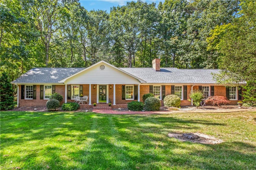 Brick ranch home with a white central gable, broad green lawn, and mature trees.