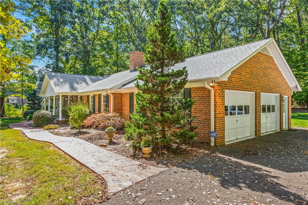 Red brick home with an attached two-car garage, curved walkway, and mature trees.