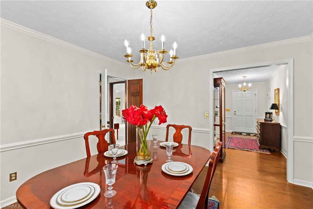 Dining room with a polished wooden table, red flowers, and a brass chandelier.