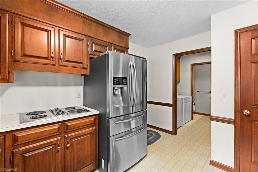 Kitchen with wood cabinets, stainless steel refrigerator, electric range, and a doorway to the laundry area.