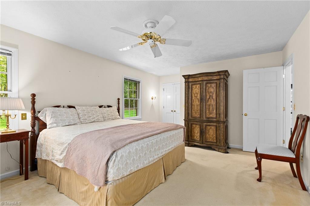 Bedroom with a large bed and ornate wooden armoire beside two windows.