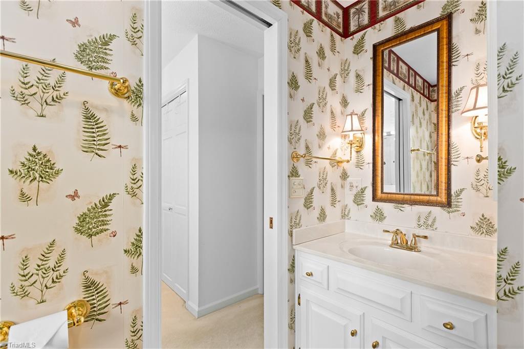 Bathroom vanity with a fern-patterned wallpaper, framed mirror, and gold-tone fixtures.