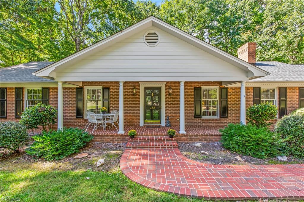 Red-brick home with a covered porch and curved brick walkway beneath mature trees.