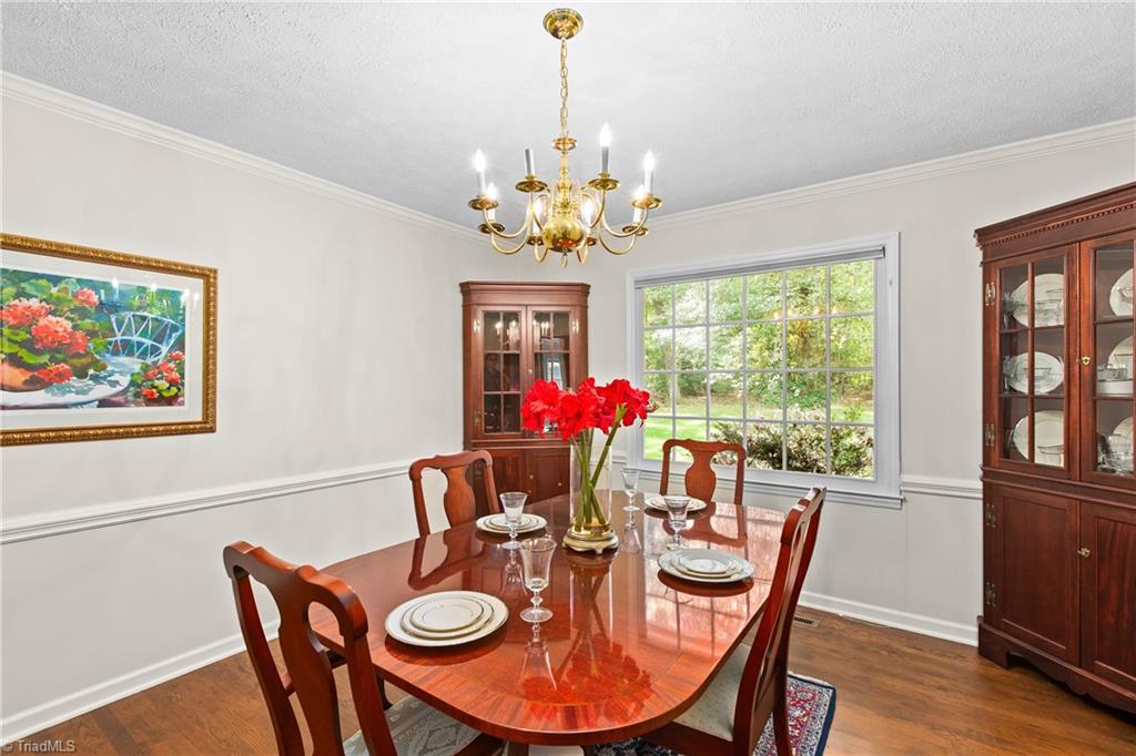 Dining room with a polished wood table, china cabinets, brass chandelier, and large garden-facing window.
