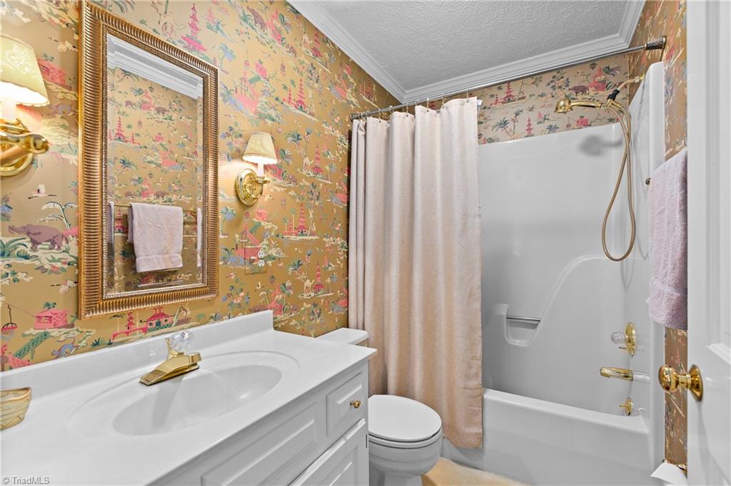 Bathroom with illustrated wallpaper, white vanity, framed mirror, and tub-shower combination.