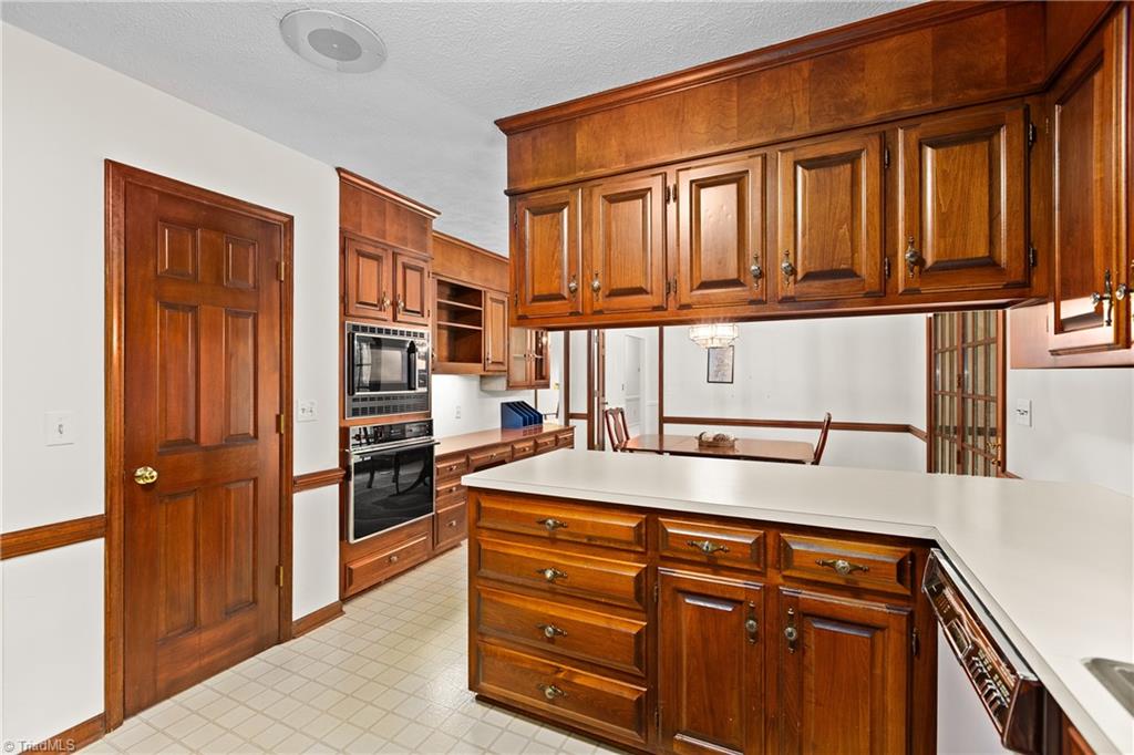 Kitchen with extensive wood cabinetry, a white island countertop, and built-in microwave and oven.