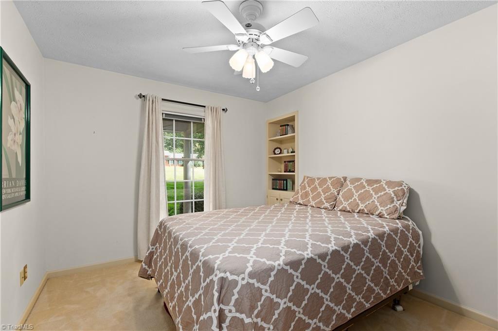 Bedroom with a patterned bedspread, ceiling fan, curtained window, and built-in shelves.