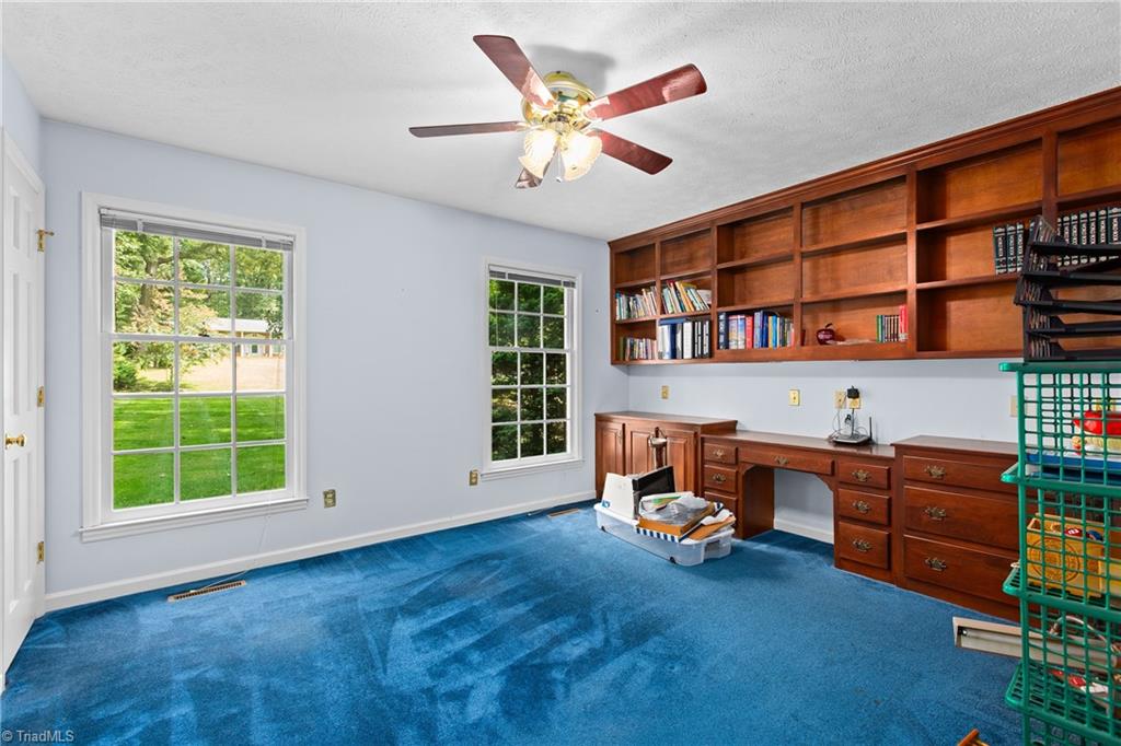 Home office with built-in wooden bookshelves and desk, blue carpet, and two windows.