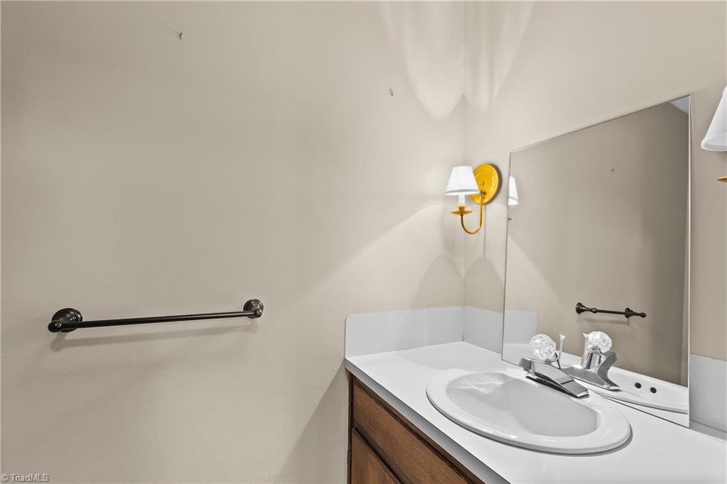 Bathroom vanity with an oval sink, wood cabinets, large mirror, and brass wall sconce.