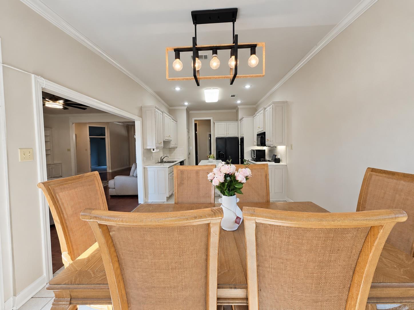 Dining area with cane-back chairs, pink flowers, and an open view into the white kitchen.