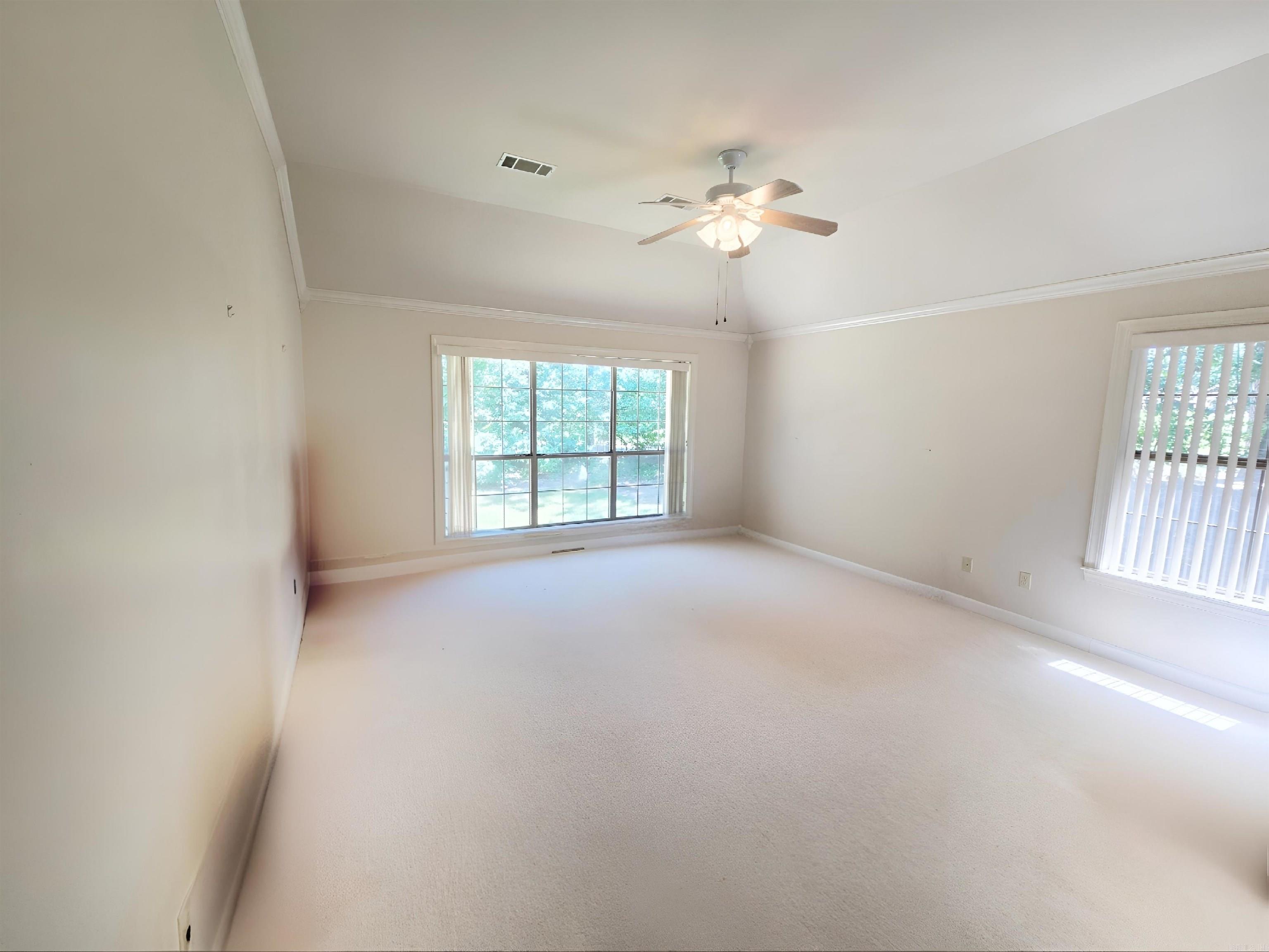 Vacant carpeted room with a vaulted ceiling, ceiling fan, and two windows.
