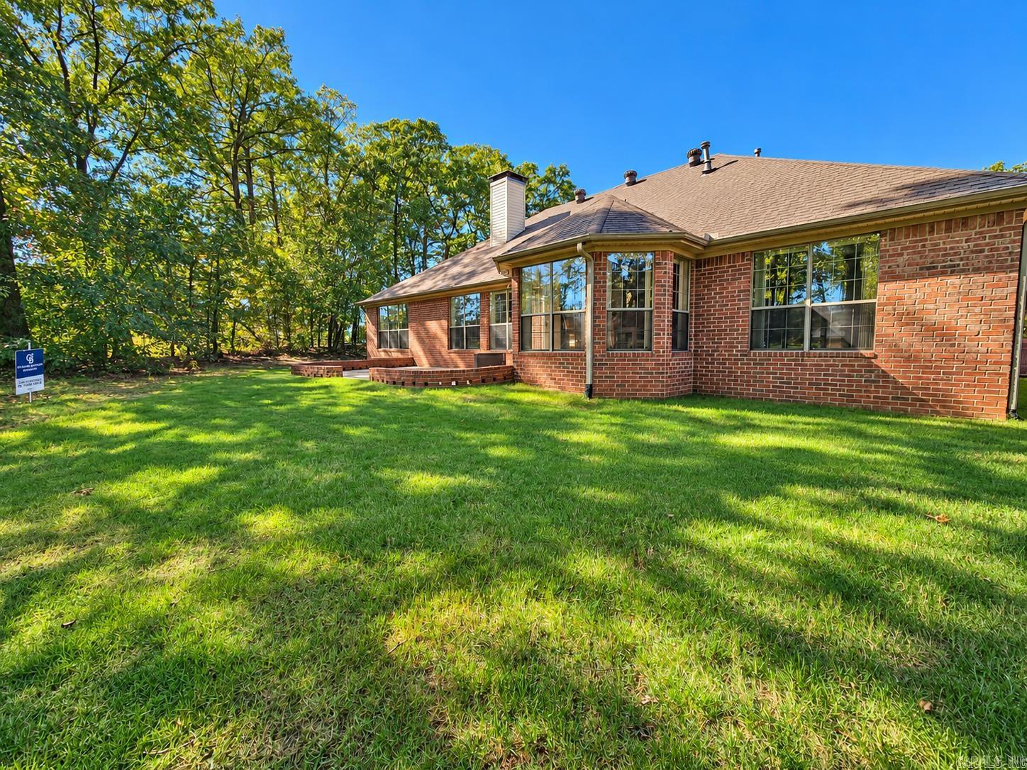 Red-brick home with large windows, a wide lawn, and mature trees behind it.