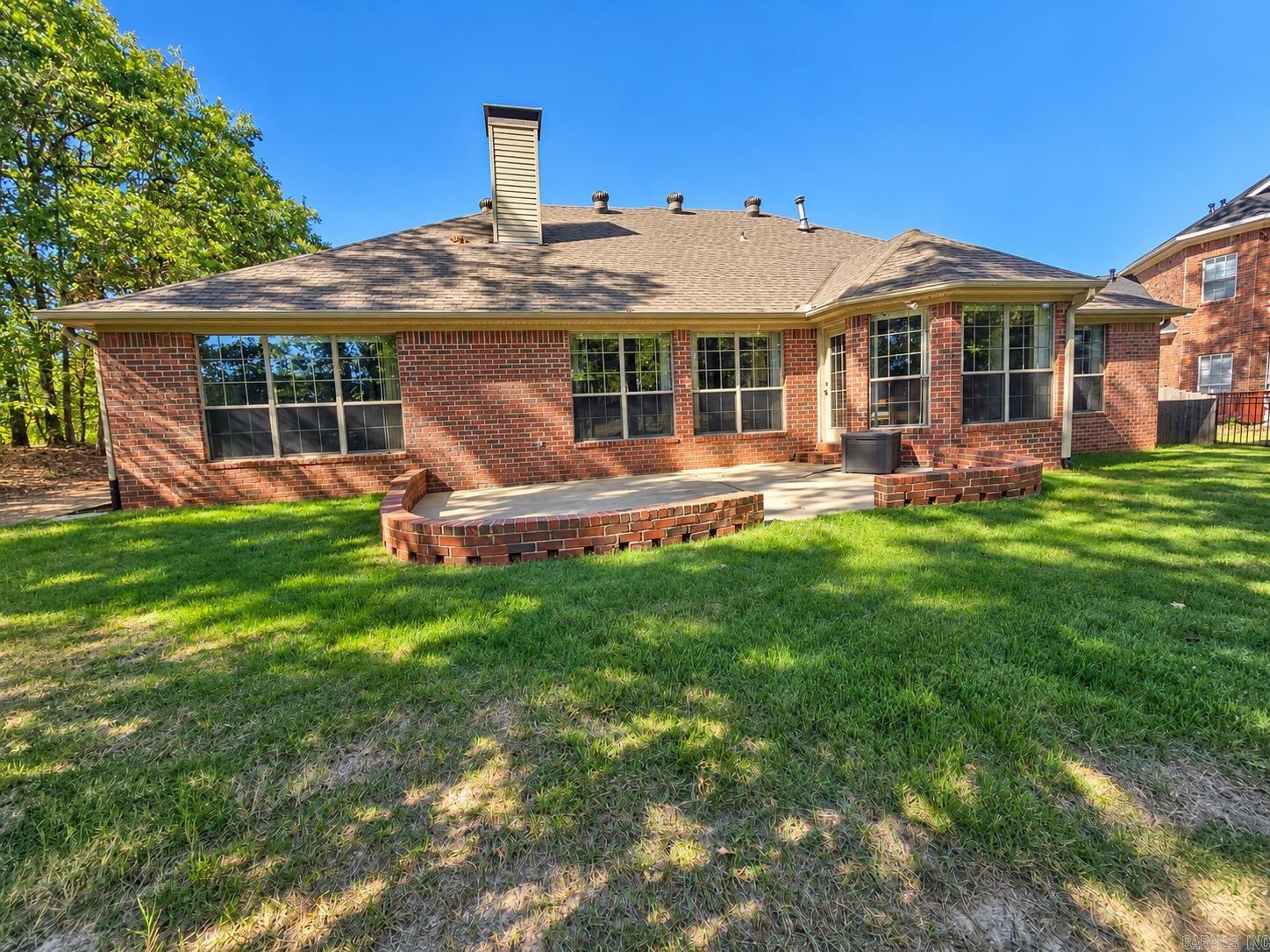 Red-brick home with a raised curved patio and a shaded grassy backyard.