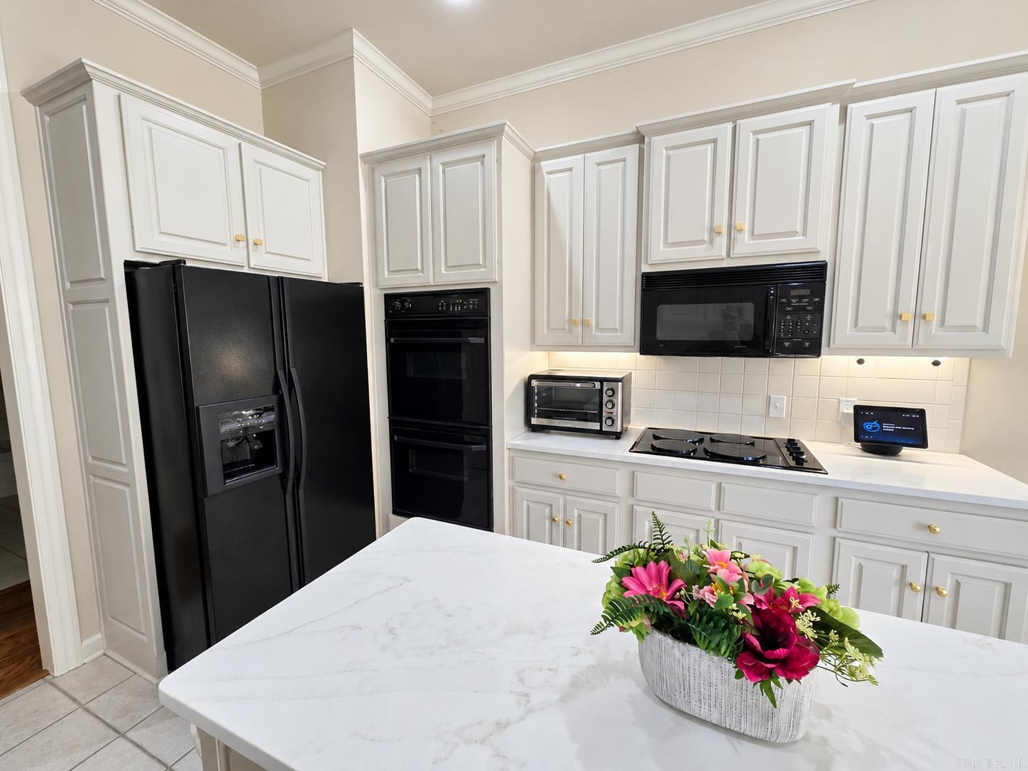 Kitchen with white cabinetry, black appliances, and a marble-look island topped with flowers.