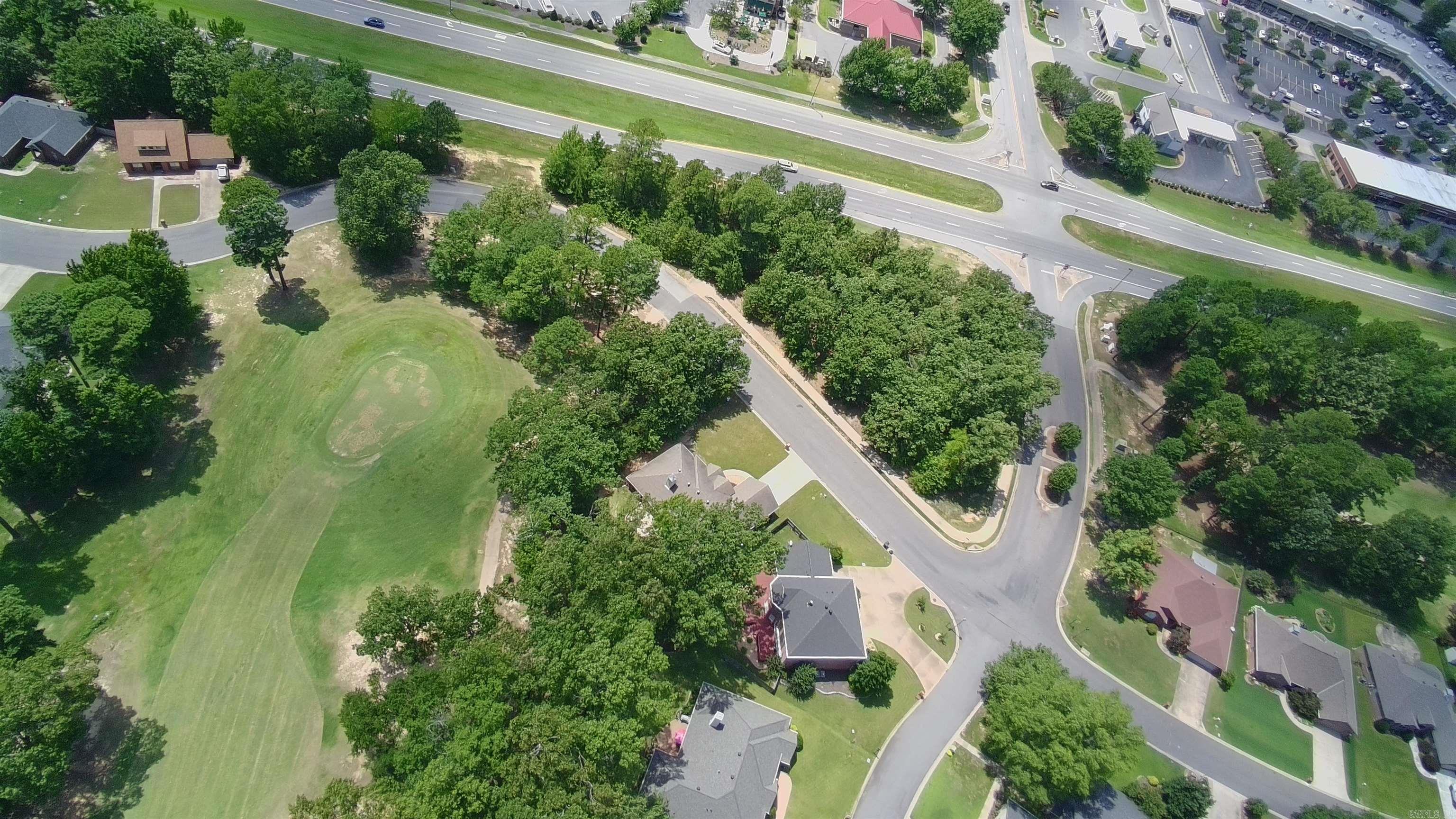 Aerial view of a tree-lined neighborhood with homes, curving streets, and a broad grassy open space.