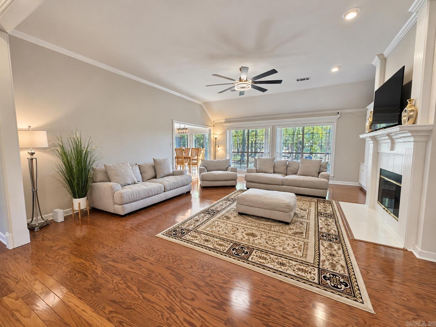 Living room with hardwood floors, neutral sofas, large windows, and a fireplace with a mounted television.