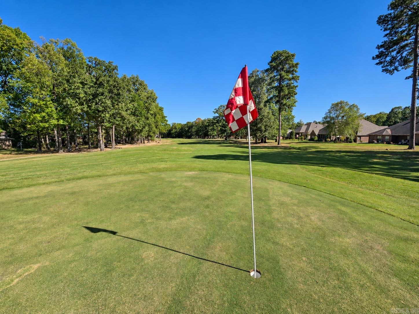 Golf course green with a red-and-white flag, mature trees, and homes along the fairway.