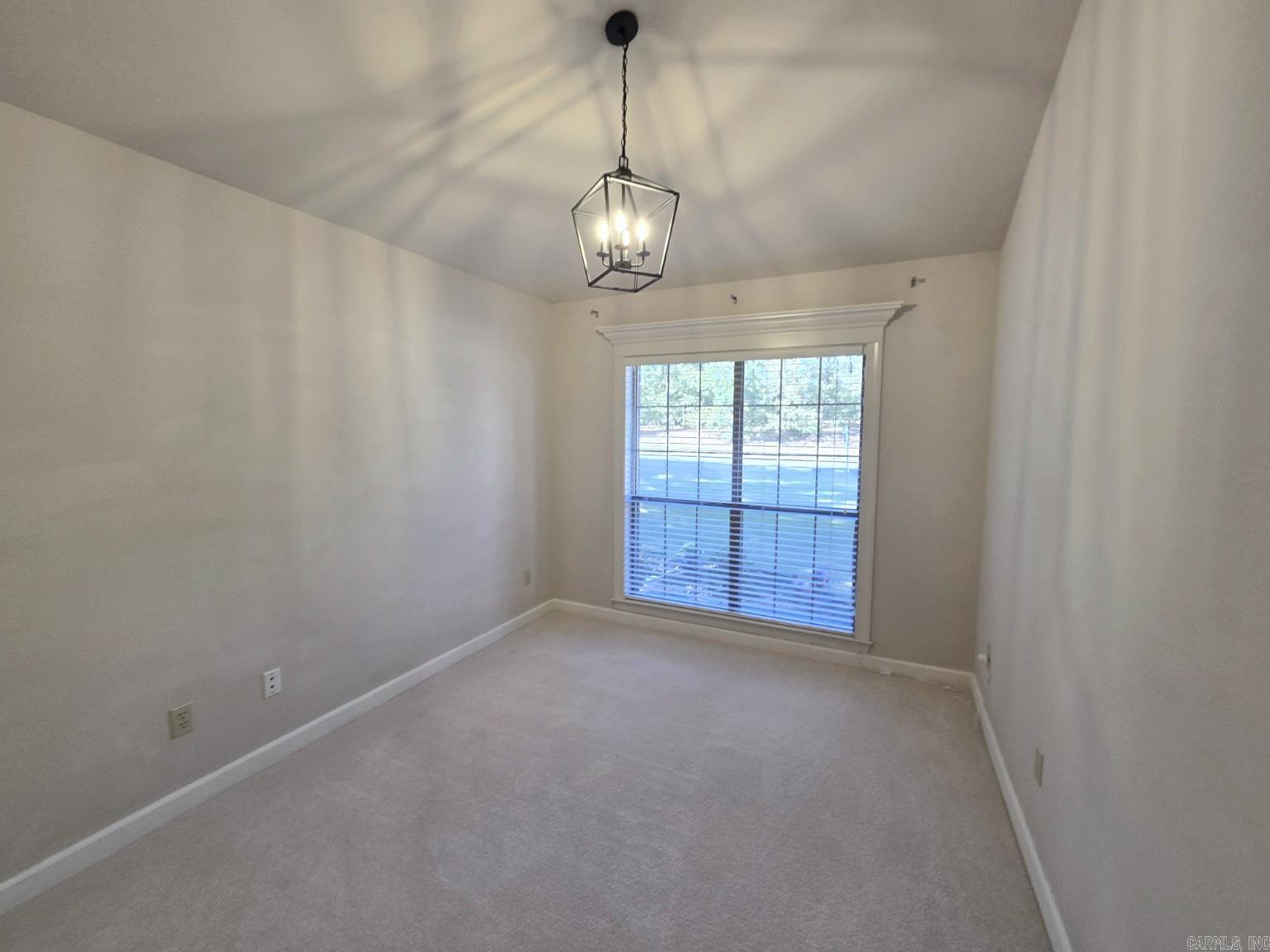 Empty carpeted room with a large window, blinds, and a geometric pendant chandelier.