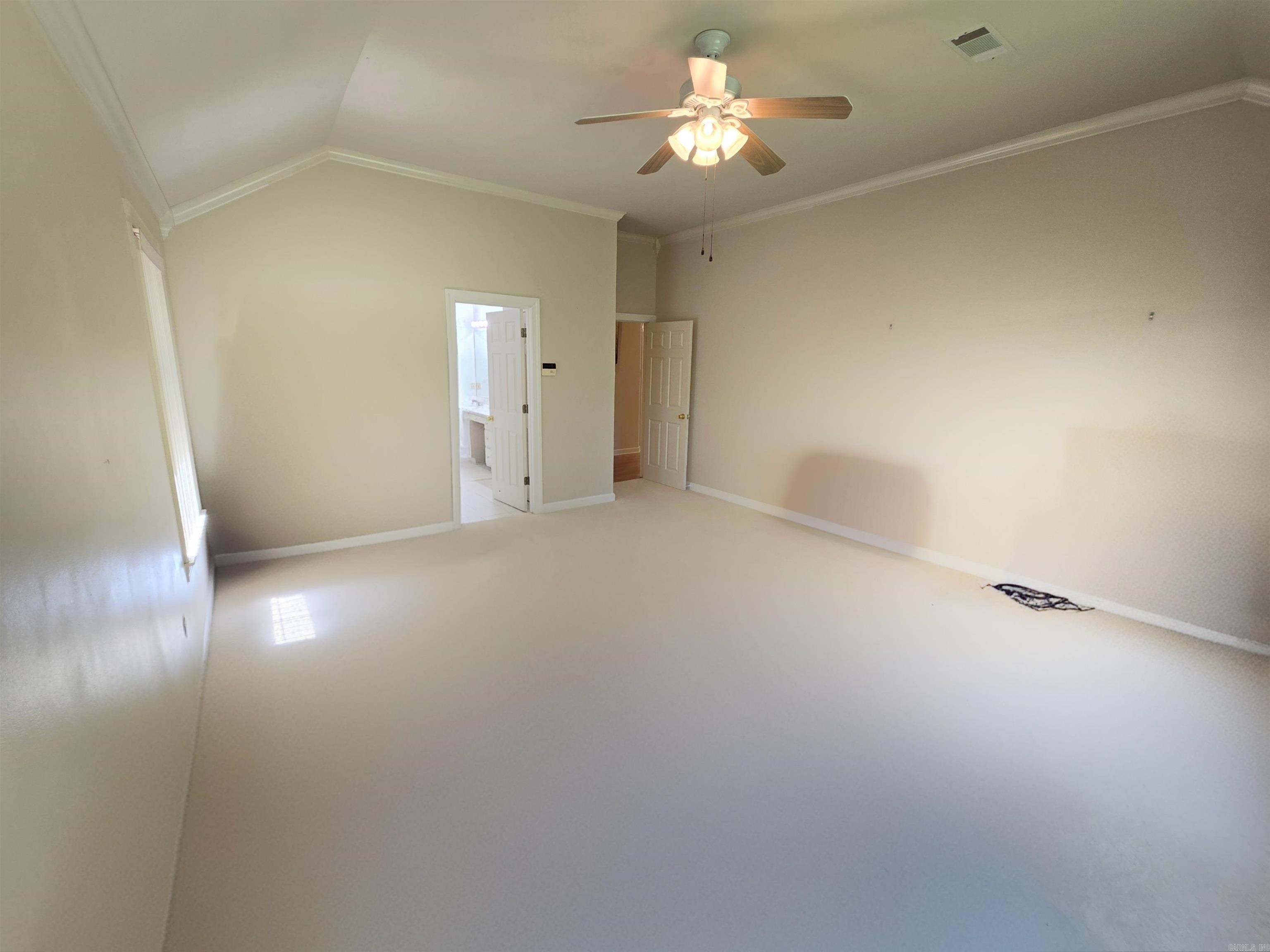 Empty bedroom with a high ceiling, lit ceiling fan, and open doorways.