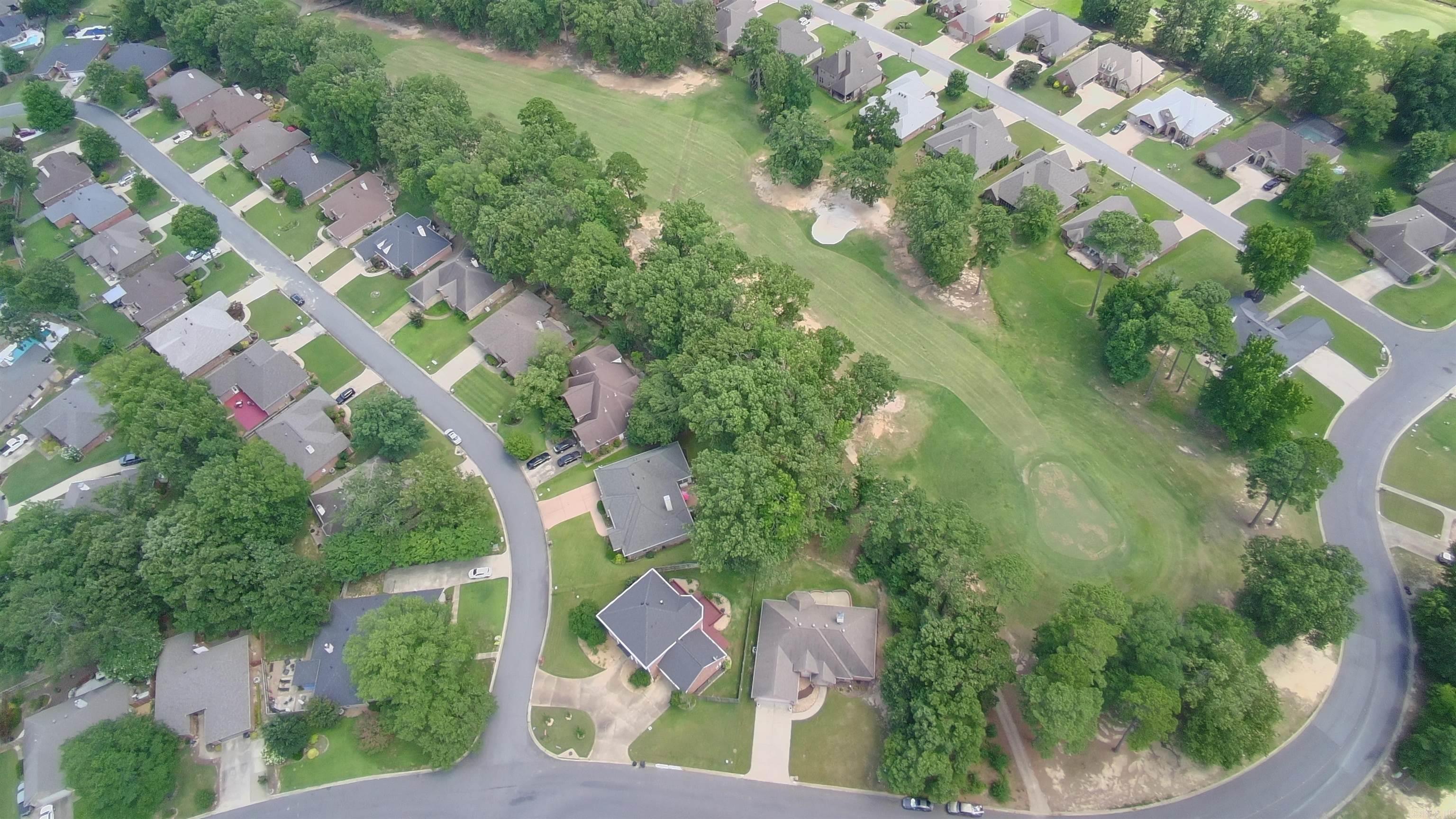 Aerial view of homes around a broad grassy open space shaded by mature trees.