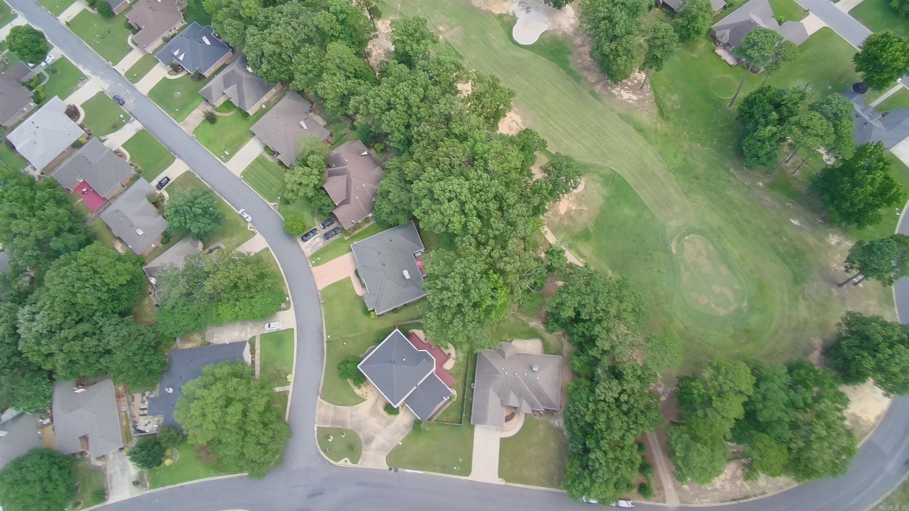 Aerial view of homes and tree-lined streets beside a large open grassy area.