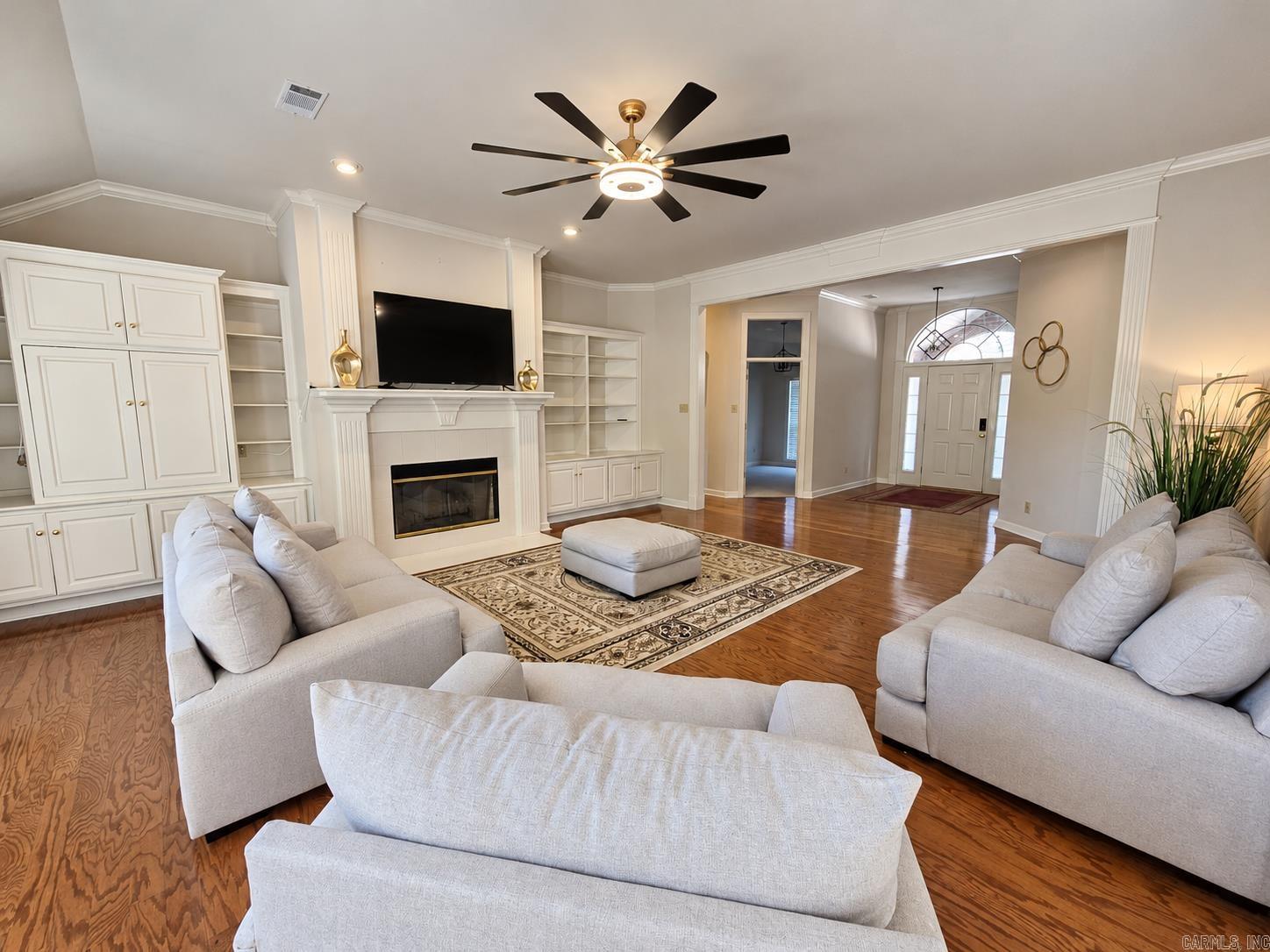 Living room with white built-ins, a fireplace, hardwood floors, and light sofas.