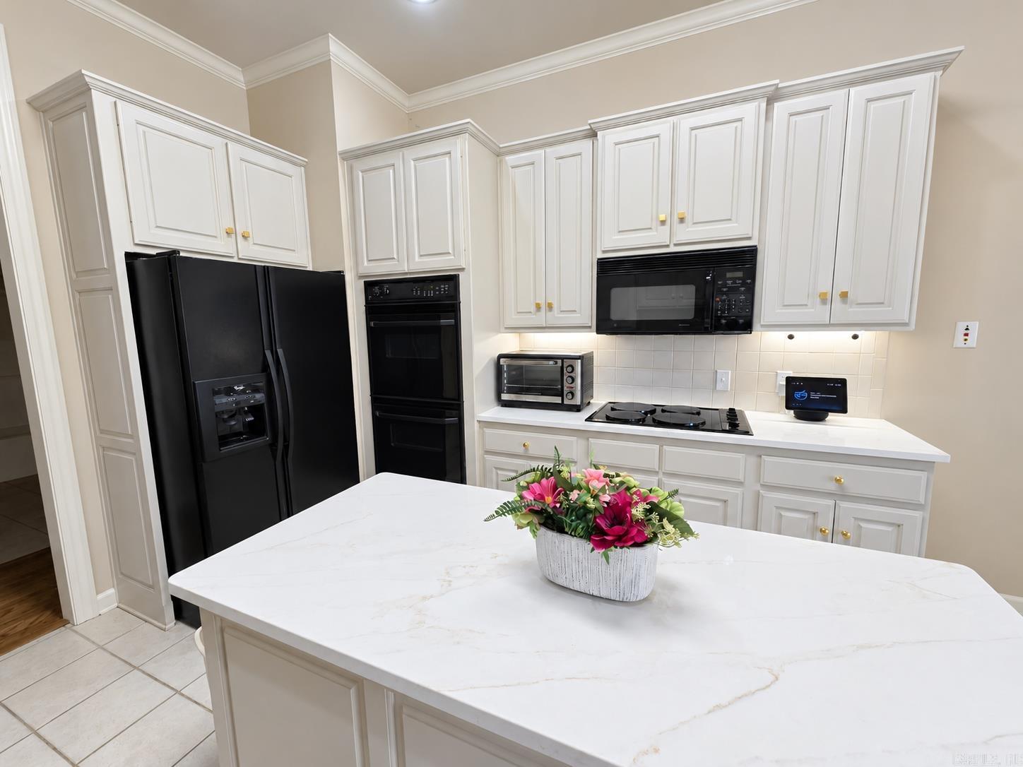 Kitchen with white cabinetry, black appliances, and a large island topped with flowers.
