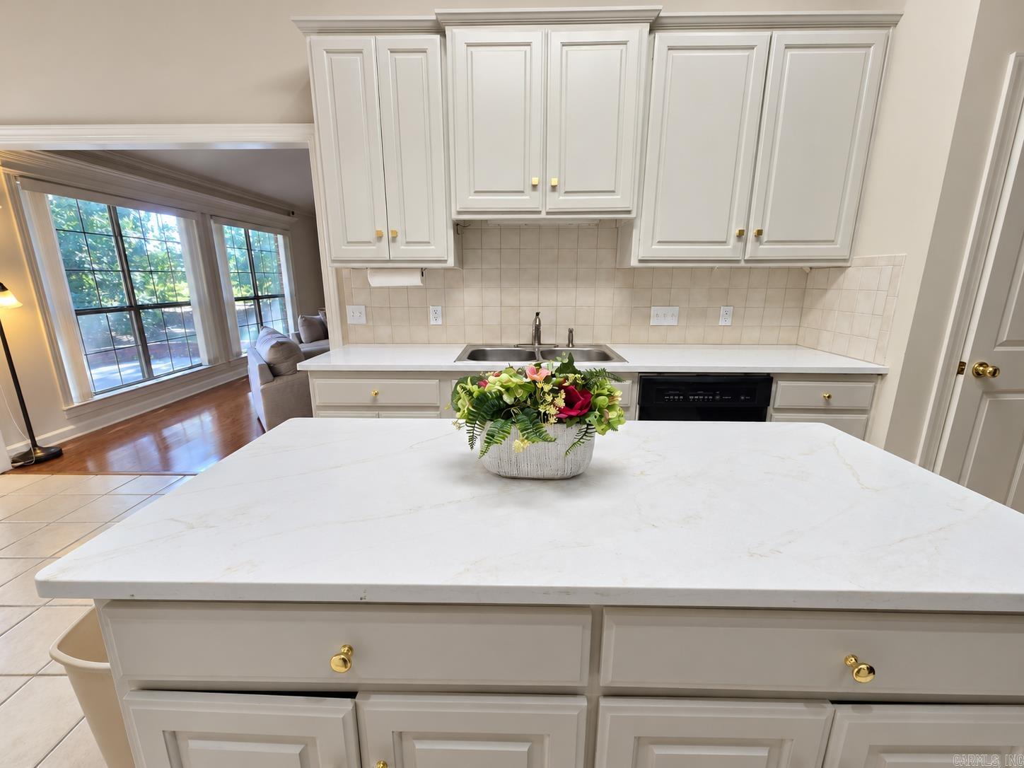 Kitchen with white cabinets, a large island, and a floral centerpiece beside a bright windowed sitting area.