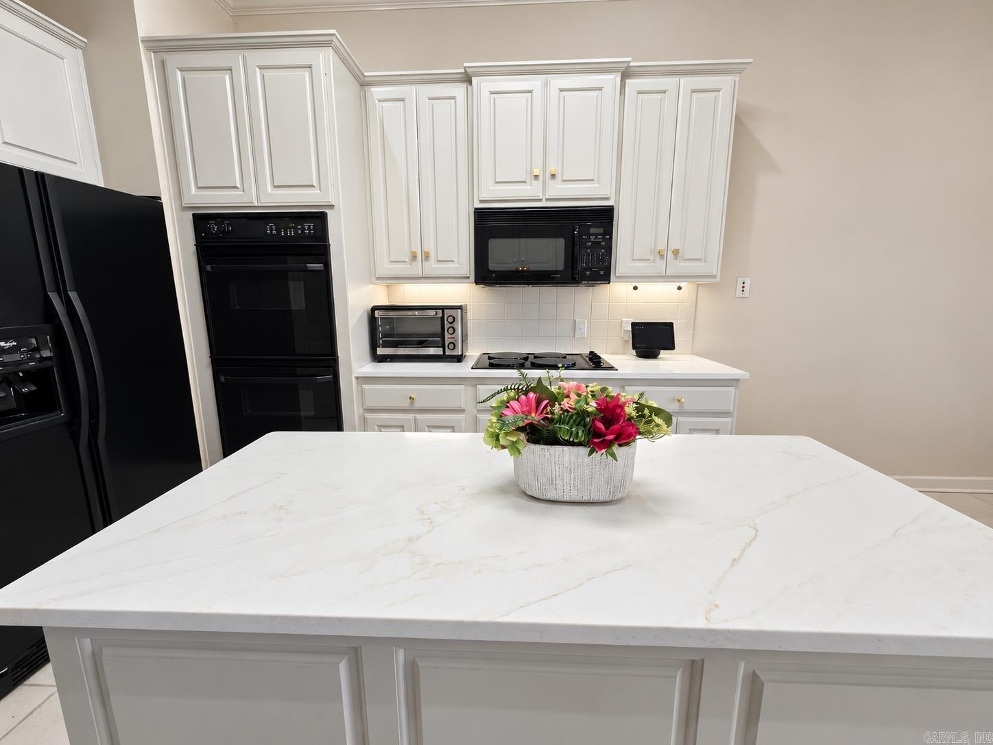 Kitchen with a large white island, white cabinetry, black appliances, and pink flowers.