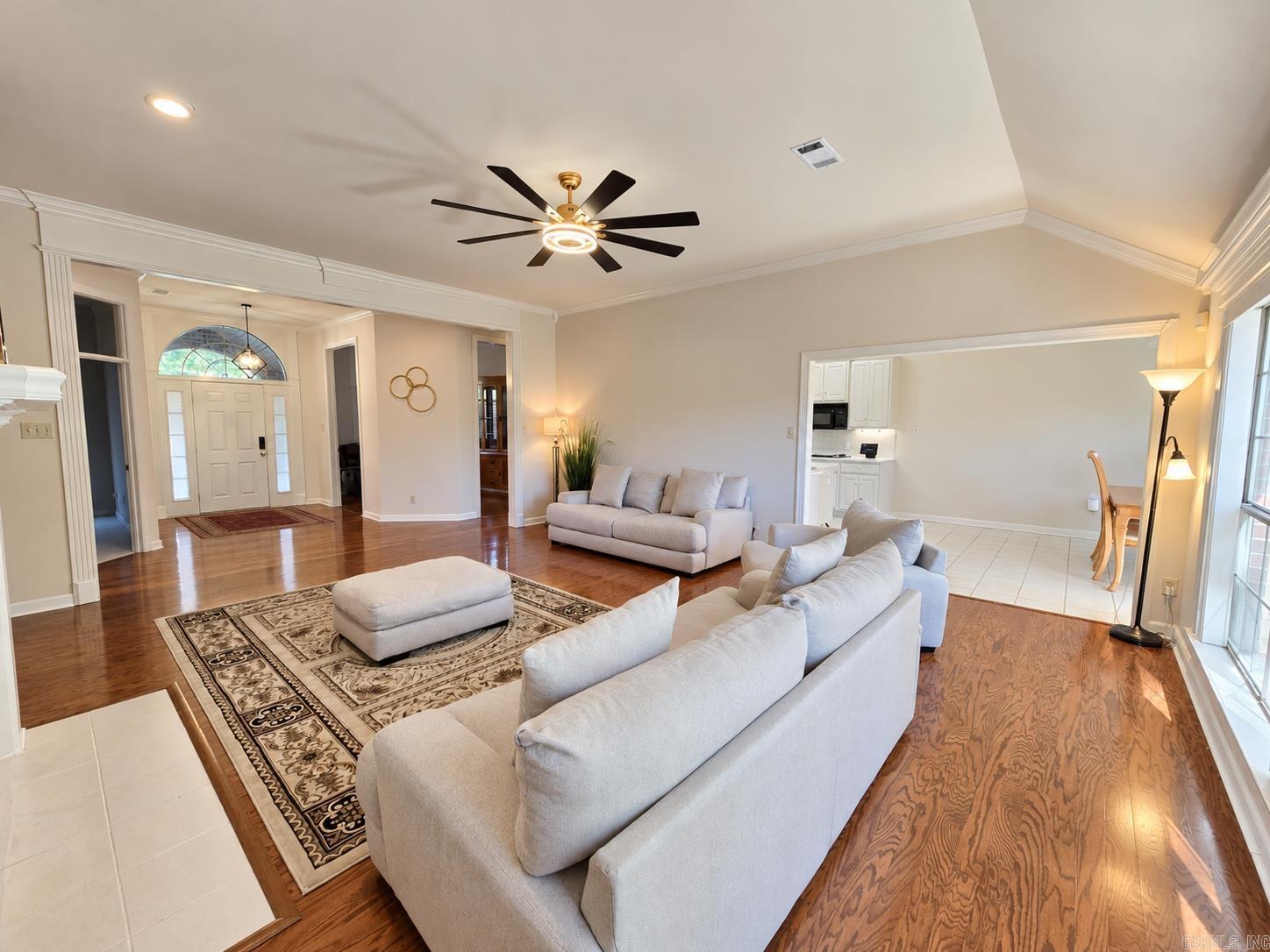 Living room with pale sofas, patterned rug, polished hardwood floors, and a view toward the front entry.