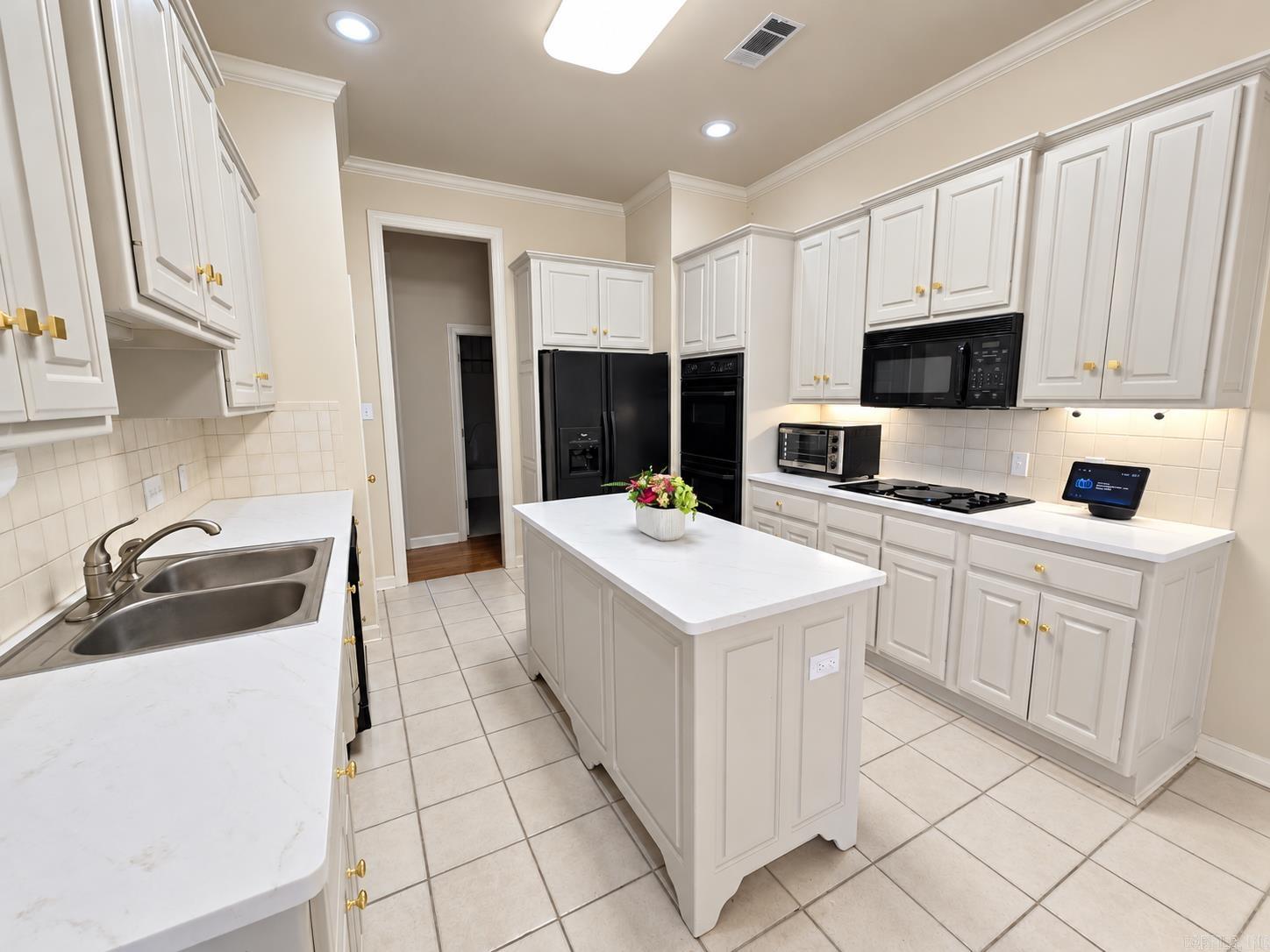 Kitchen with white cabinets, a large island, black appliances, and a double-basin sink.