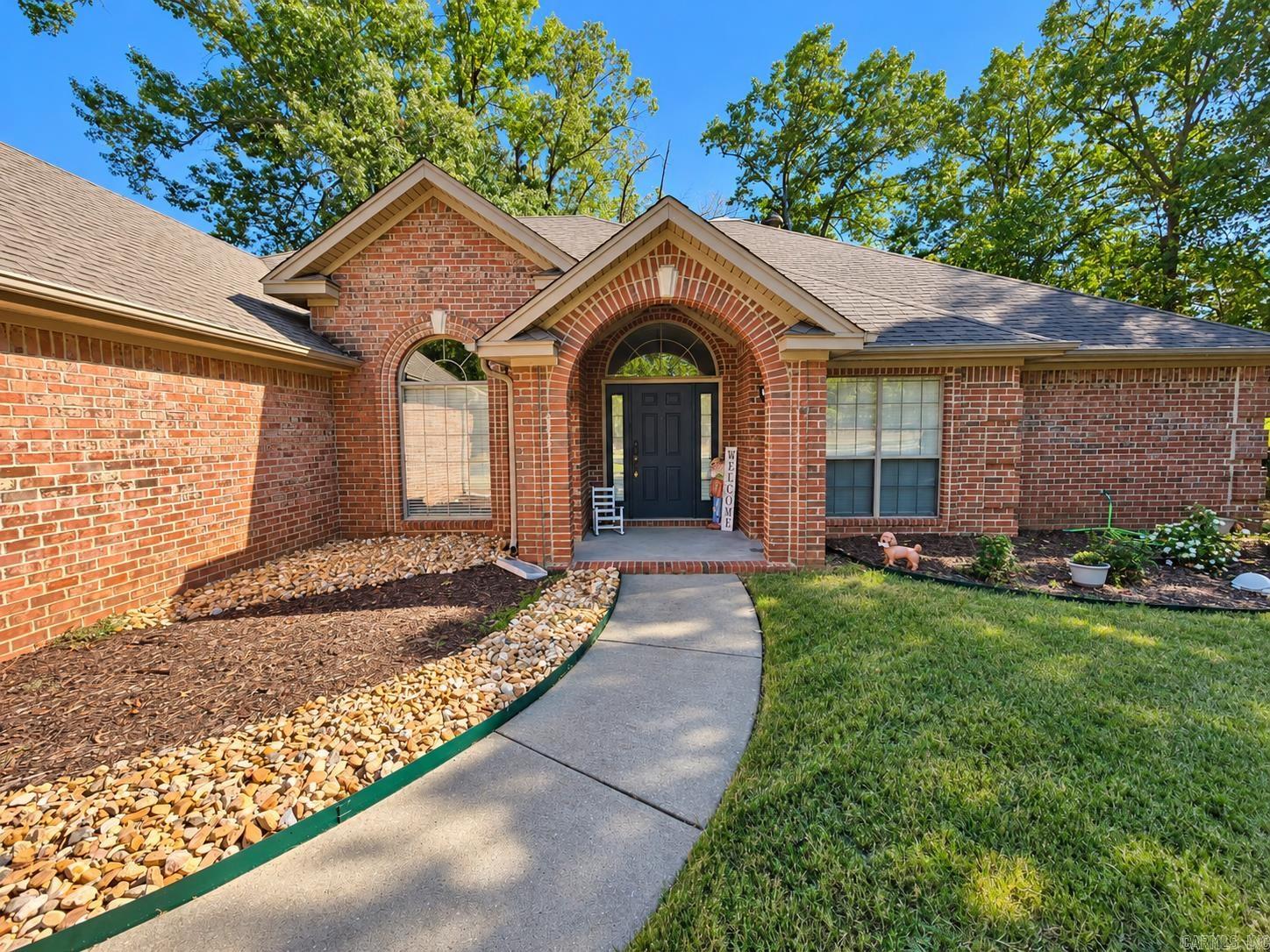 Red brick home with an arched entry, curved walkway, landscaped beds, and front lawn.