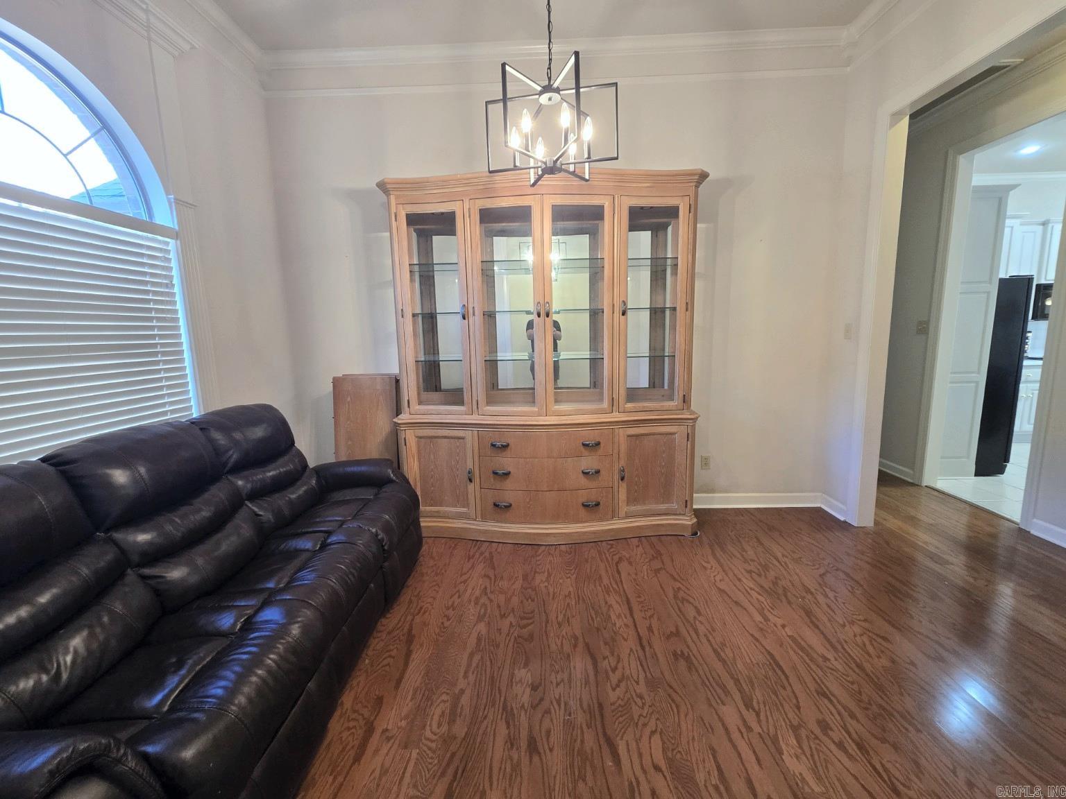 Living room with a leather sectional, glass-front wood cabinet, hardwood floors, and an arched window.