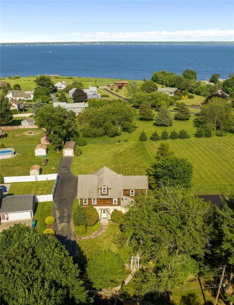 Aerial view of a shingled home, broad lawn, and waterfront beyond.