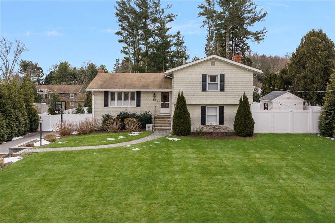 Split-level home with dark shutters, a white fence, and a broad lawn with patches of snow.