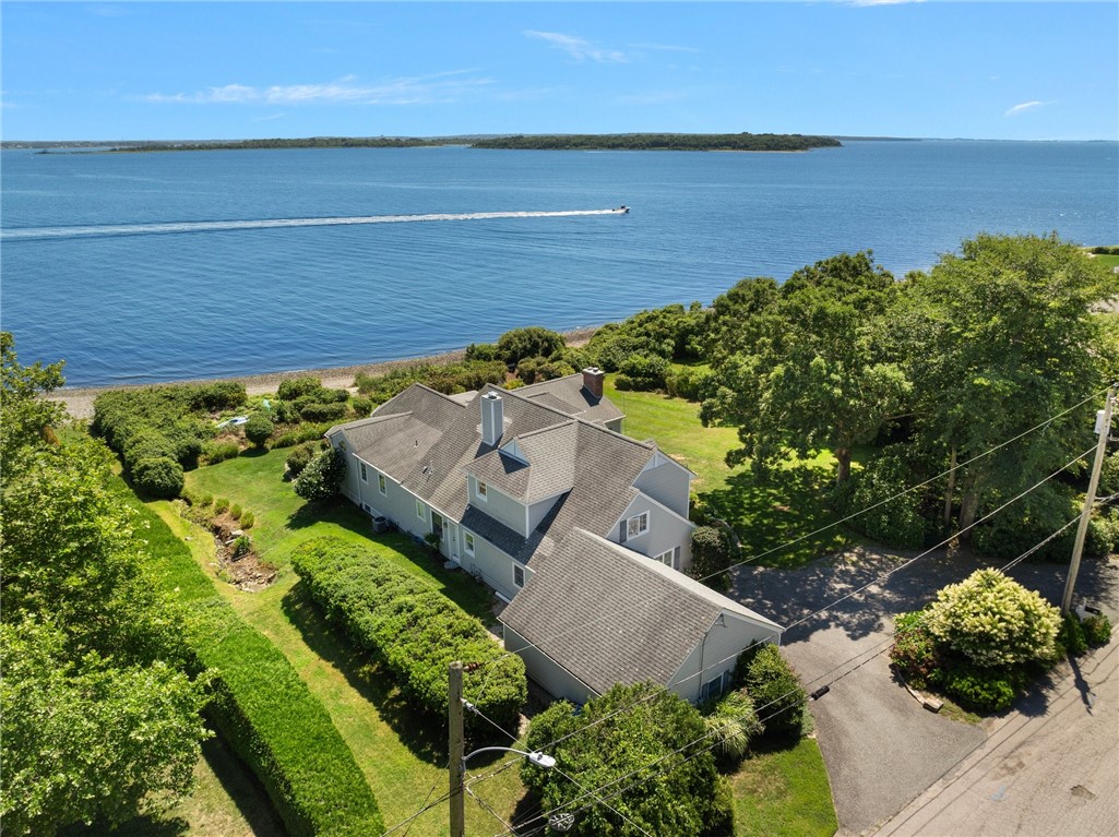 Waterfront house with a landscaped yard overlooking blue water and a distant shoreline.