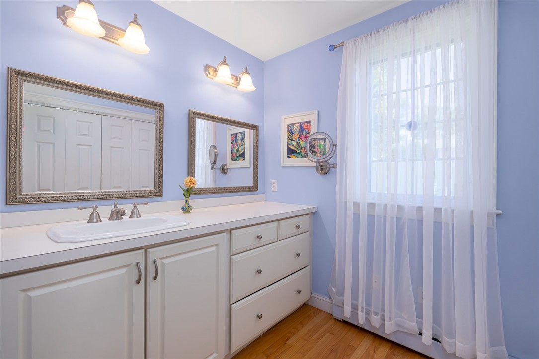 Bathroom vanity with a long white countertop, ornate mirrors, and a tall curtained window.