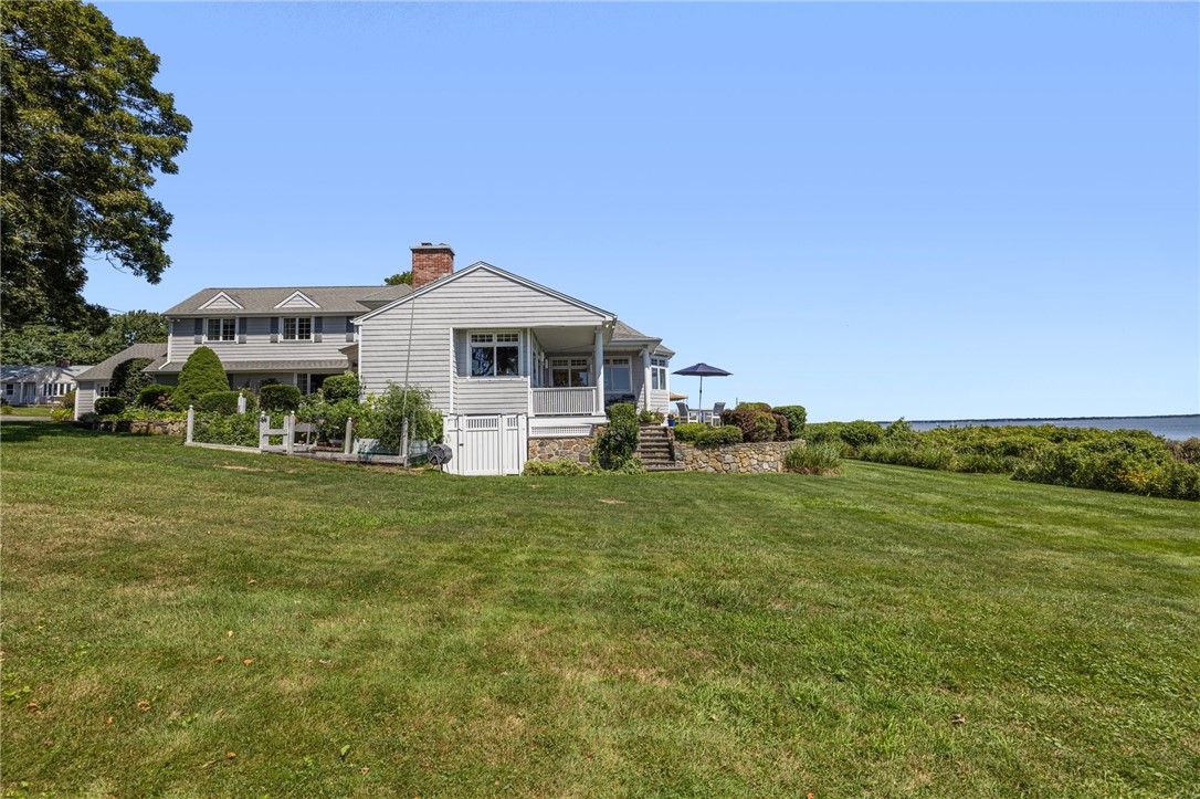 Gray shingle-sided house with a covered porch, broad lawn, and water view.