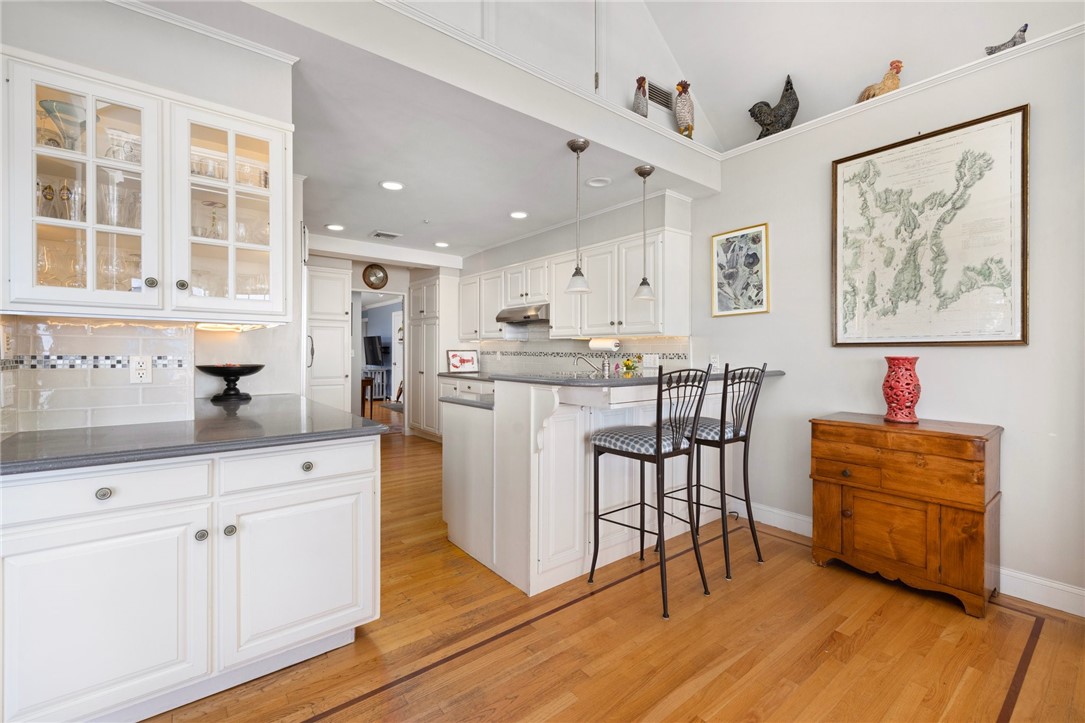 Kitchen with white cabinetry, a breakfast bar, hardwood floors, and a framed map.