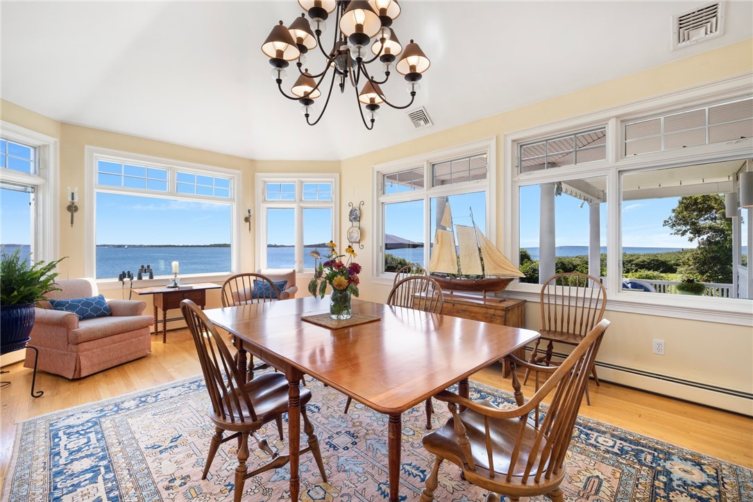 Dining room with a large wooden table and chairs, overlooking the water through expansive windows.