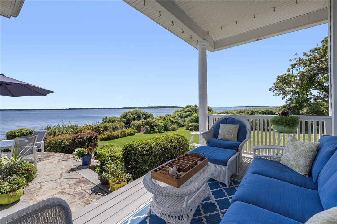 Covered waterfront porch with blue cushioned seating overlooking landscaped gardens and the water.