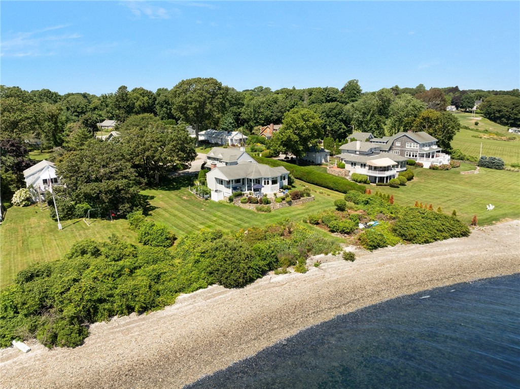 Coastal home with landscaped lawn, neighboring houses, and a rocky shoreline.