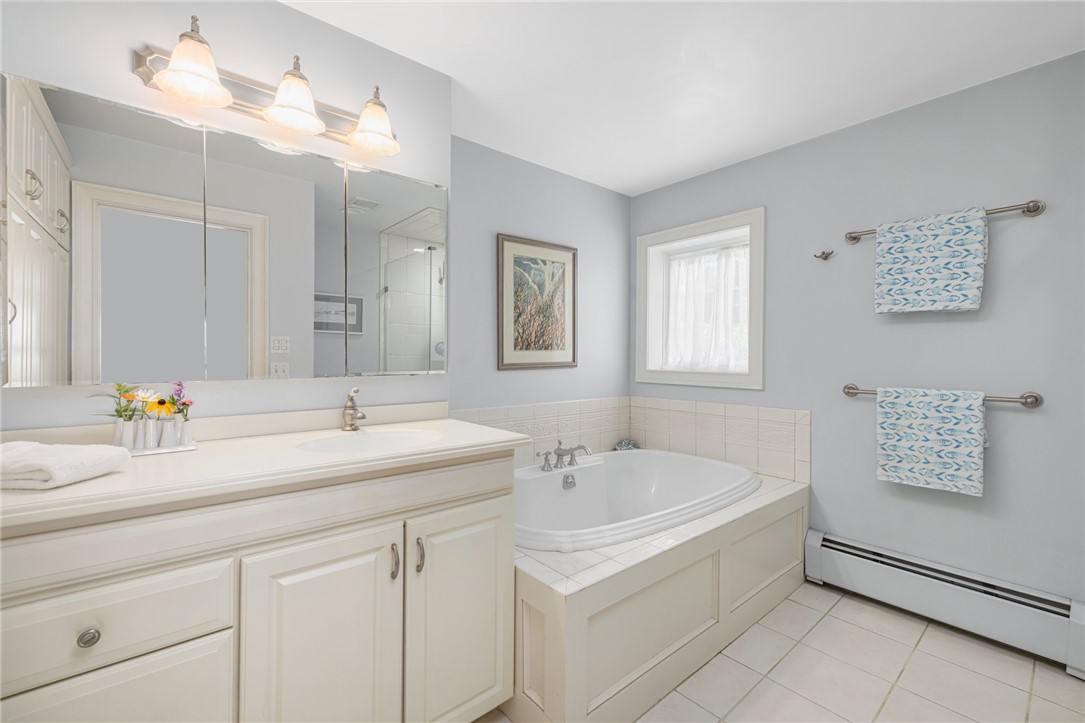 Bathroom with a white vanity, large mirror, and corner soaking tub beneath a window.