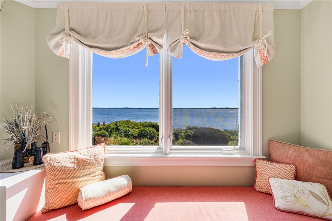 Window seat with coral cushions overlooking shrubs and a broad expanse of water.