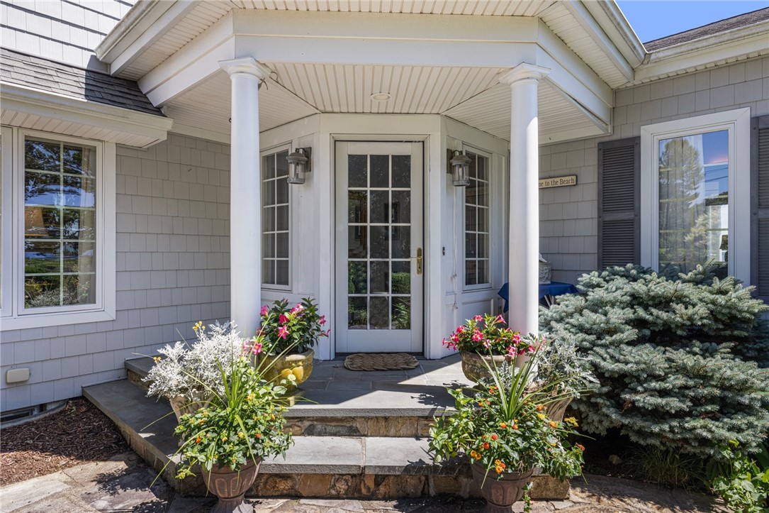 Home entrance with white columns, a glass-paneled door, stone steps, and colorful potted flowers.