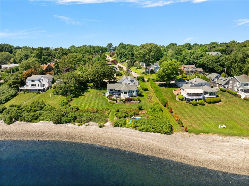 Aerial view of waterfront homes, lawns, a tree-lined neighborhood, and a pebbled beach.
