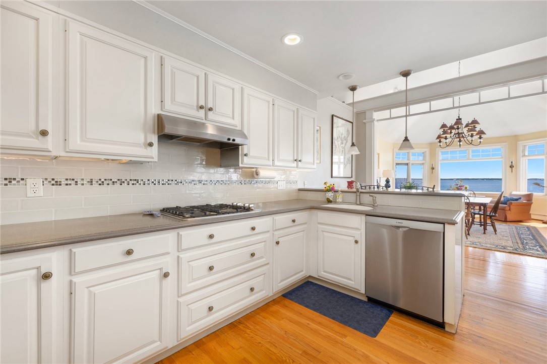 White kitchen with a gas cooktop and stainless dishwasher, opening to a dining area overlooking the water.