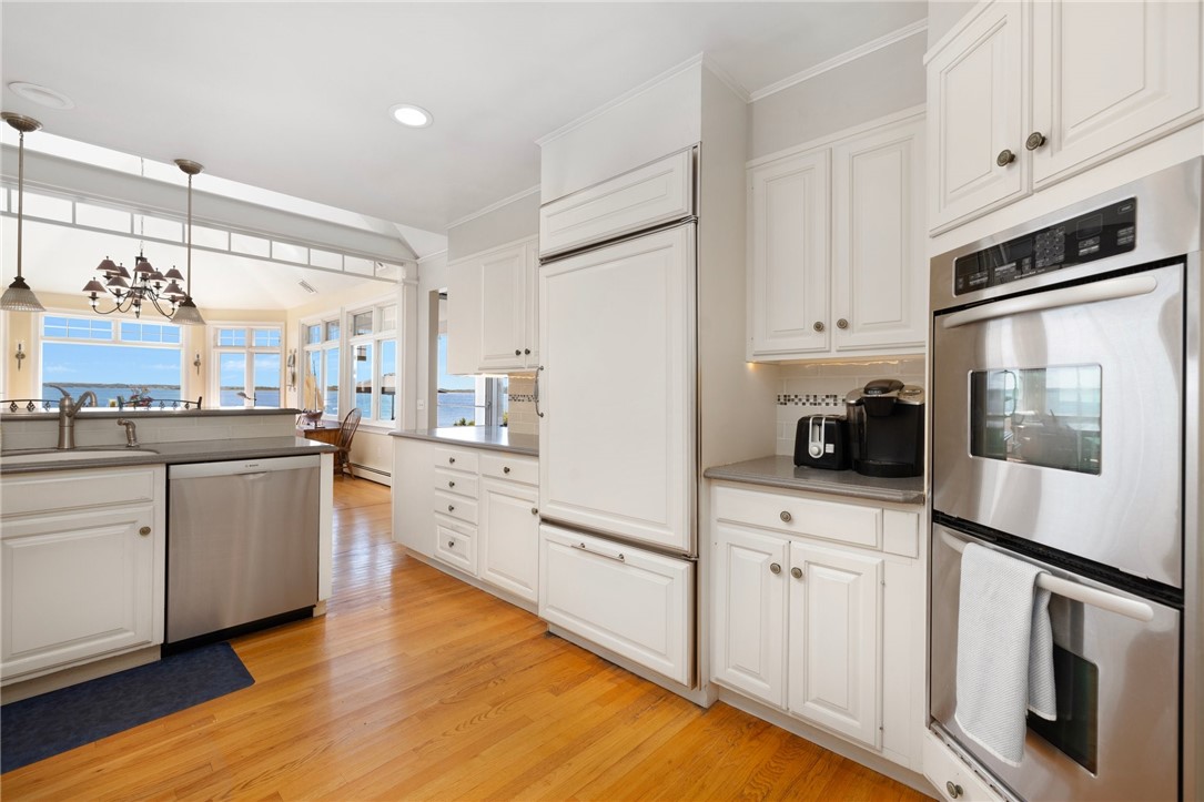 White kitchen with stainless appliances and hardwood floors, opening to windows overlooking the water.