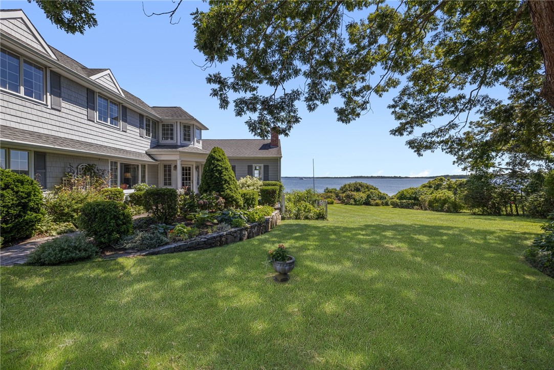 Shingled waterfront home beside a broad lawn, with landscaped gardens and water views.